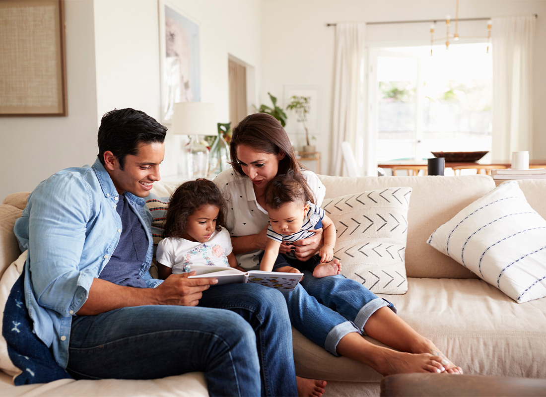 Personal Insurance.- Young Family Relaxing and Reading a Book Together on the Sofa